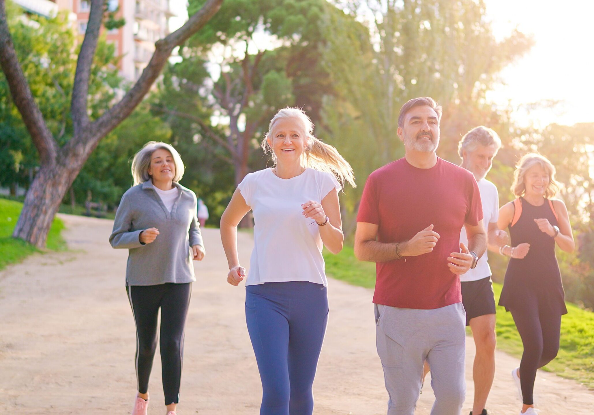 Five active mature adults jogging together on a sunny day, focusing on health and friendship